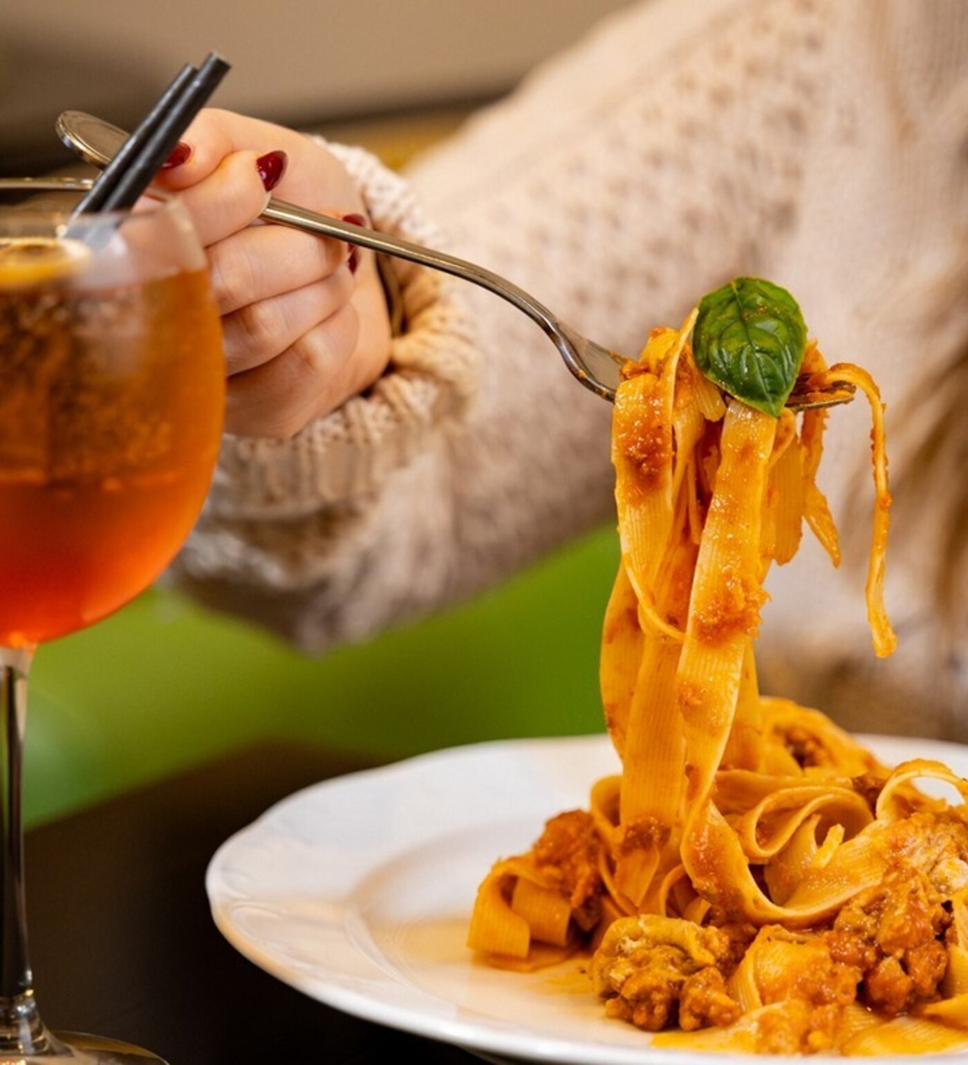 Tagliatelle al ragù being lifted with a fork, Aperol spritz in the foreground
