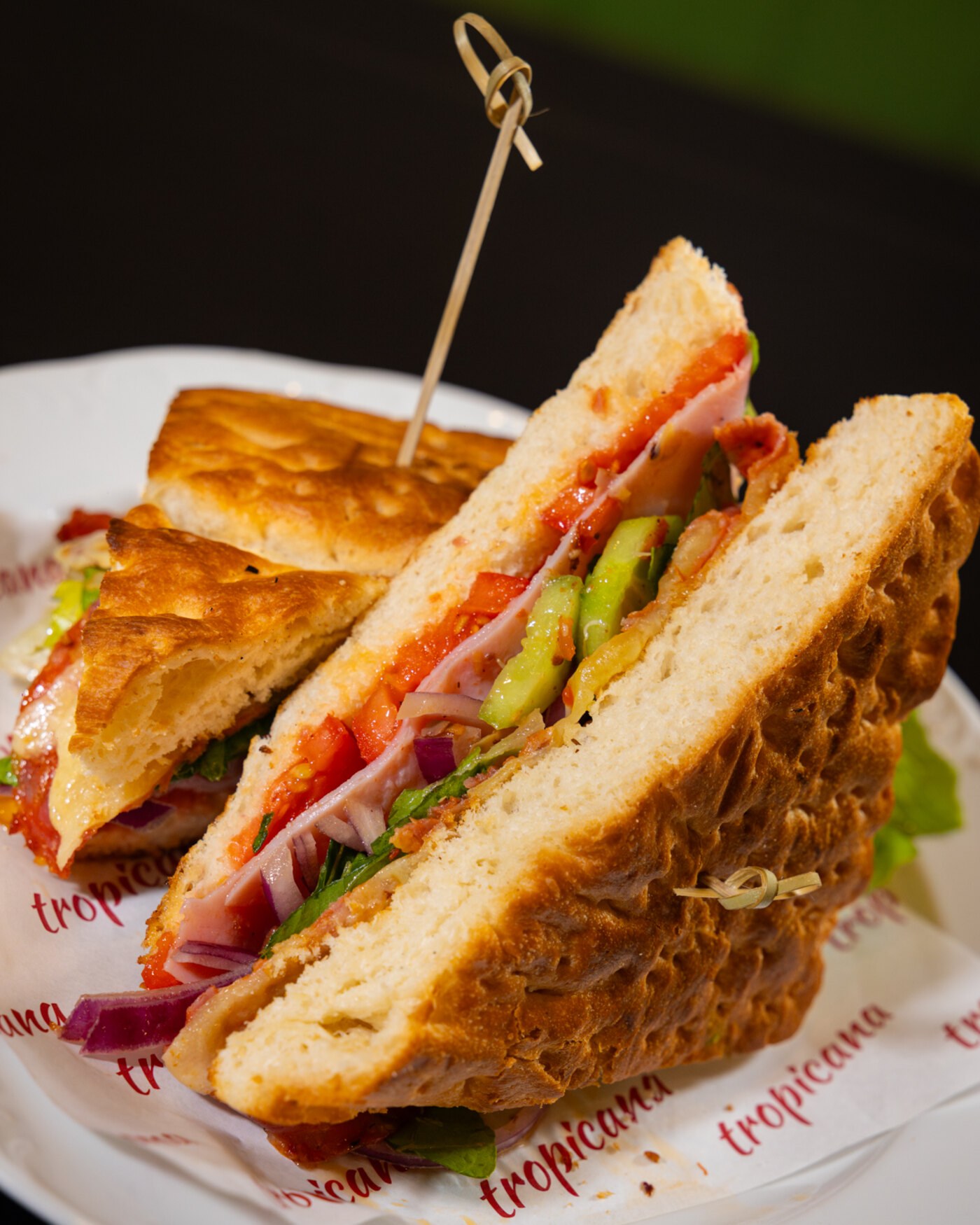 Focaccia panini stacked with prosciutto, tomato and salad on Tropicana branded paper