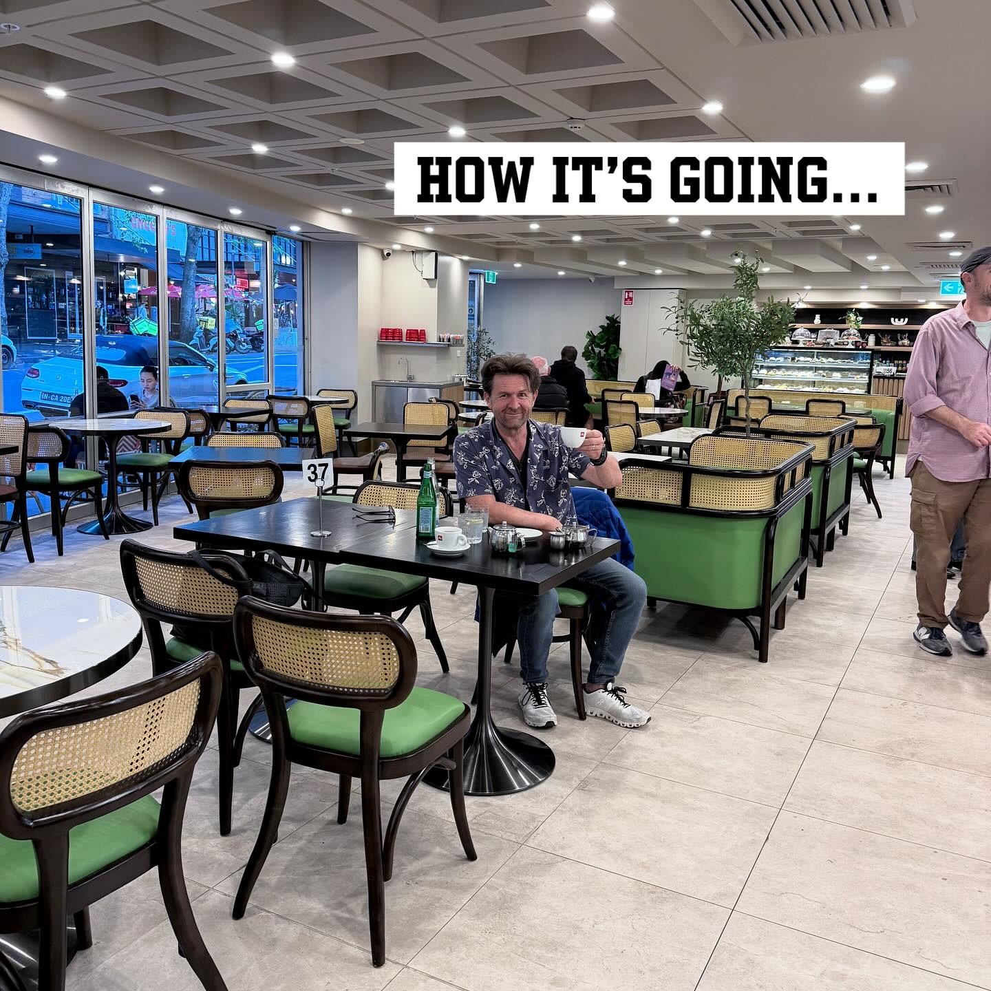 John Polson back at Tropicana Caffe this year, seated with a coffee in the renovated room with green upholstered chairs, graphic overlay reading HOW IT'S GOING